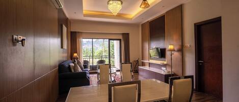 A hotel room with a dining area, a sofa, a TV, and a large window.