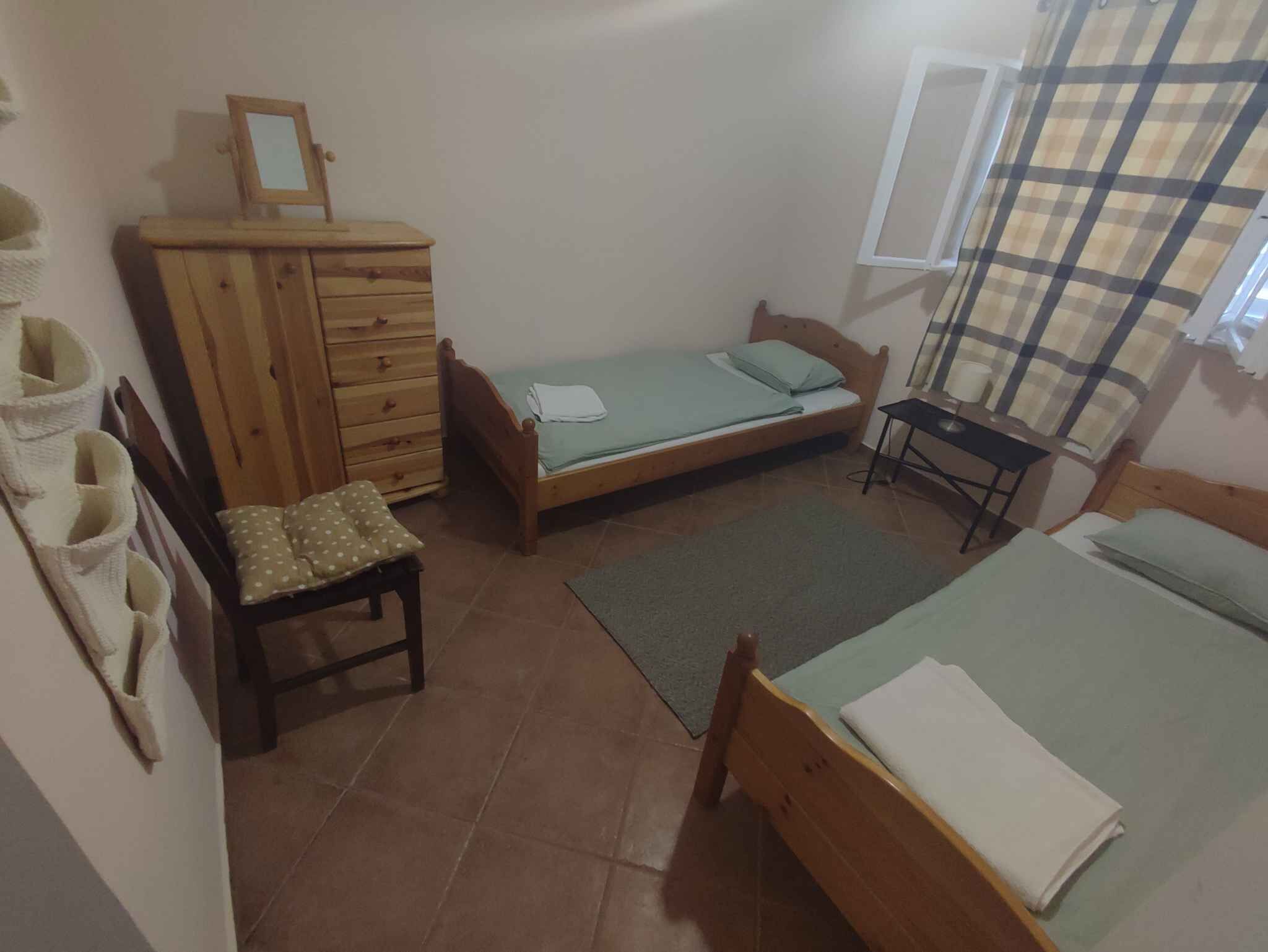 A small, tidy bedroom with a single bed, a wooden dresser, a chair, and a desk.