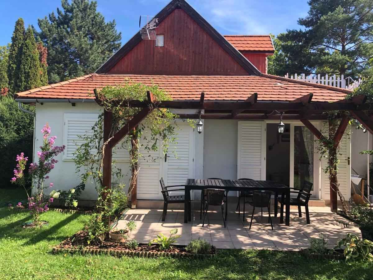 A house with a red roof, a covered patio with a table and chairs, and a garden with flowering plants.