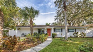 A single-story house with a red front door, white exterior, and a front yard with a pathway leading to the entrance. - Arlington Park House Sarasota Tropical Oasis
Sarasota cert of reg # VR25-00010 (Sarasota)
