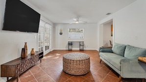 A living room with a flat-screen TV, a woven ottoman, a light green sofa, and a console table with vases. - Arlington Park House Sarasota Tropical Oasis
Sarasota cert of reg # VR25-00010 (Sarasota)