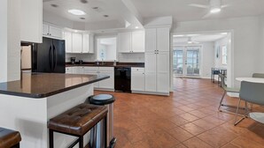 A spacious kitchen with white cabinets, a black refrigerator, and a brown countertop. There is a bar stool and a trash can. - Arlington Park House Sarasota Tropical Oasis
Sarasota cert of reg # VR25-00010 (Sarasota)