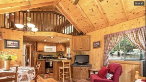 Interior acogedor de una cabaña con cocina, comedor y sala de estar que incluye una butaca roja y un televisor.