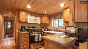 Una cocina de estilo cabaña de madera con una isla central, electrodomésticos de acero inoxidable y una ventana con cortinas a cuadros.