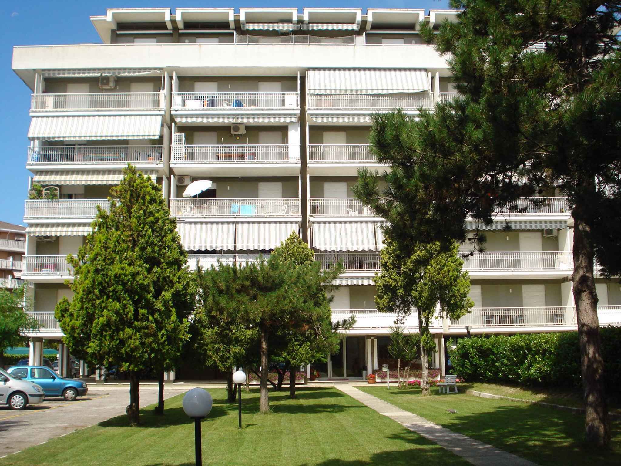 Un edificio residencial de varios pisos con balcones, un césped cuidado y automóviles estacionados.