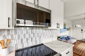 A modern kitchen with white cabinets, a stainless steel range hood, and a hexagonal tile backsplash.