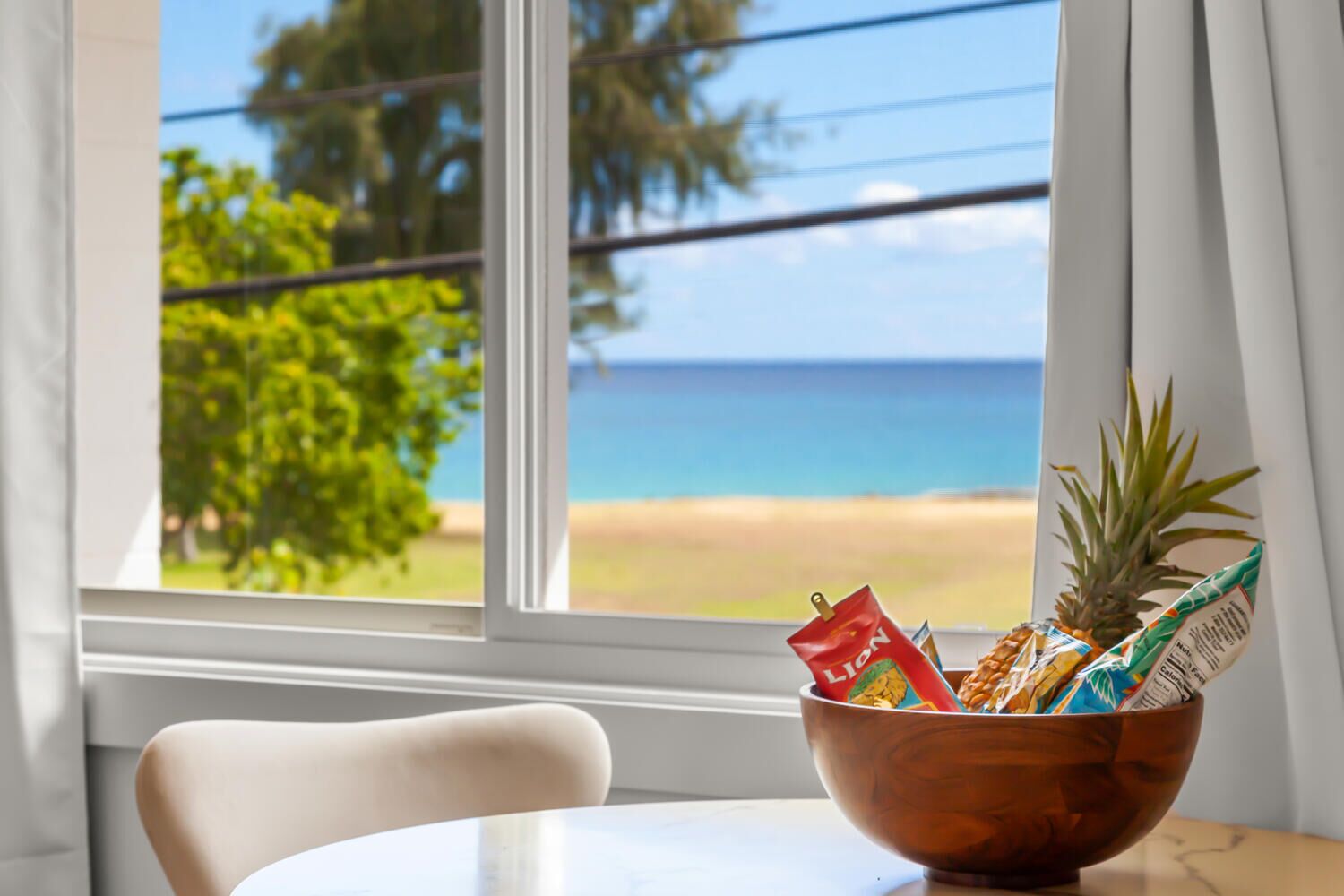 Un tazón de madera sobre una mesa junto a una ventana con vista a una playa y al océano.