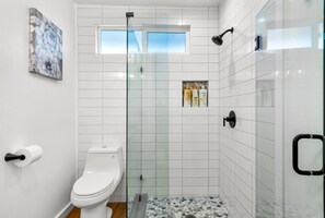A modern bathroom with a toilet, a glass shower enclosure, and a small window. - koolkondo Springwater 2 bedroom Oceanfront home (Koloa)