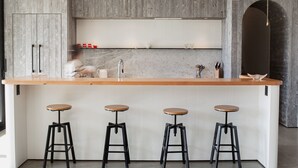 Una cocina moderna con encimera de madera, cuatro taburetes y salpicadero de mármol.