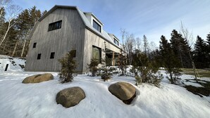 Una casa moderna de estilo granero, con techo inclinado, ventanas amplias y cimientos de piedra.