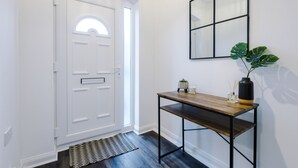 Ein Flur mit einer weißen Tür, einem Holztischchen mit Vase und Pflanze sowie einem Wandspiegel.