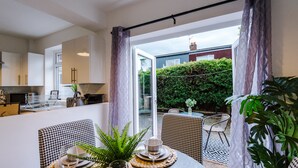 Ein Essbereich mit Tisch für vier Personen, Blick auf den Garten und einer Schiebeglastür zum Außenbereich.