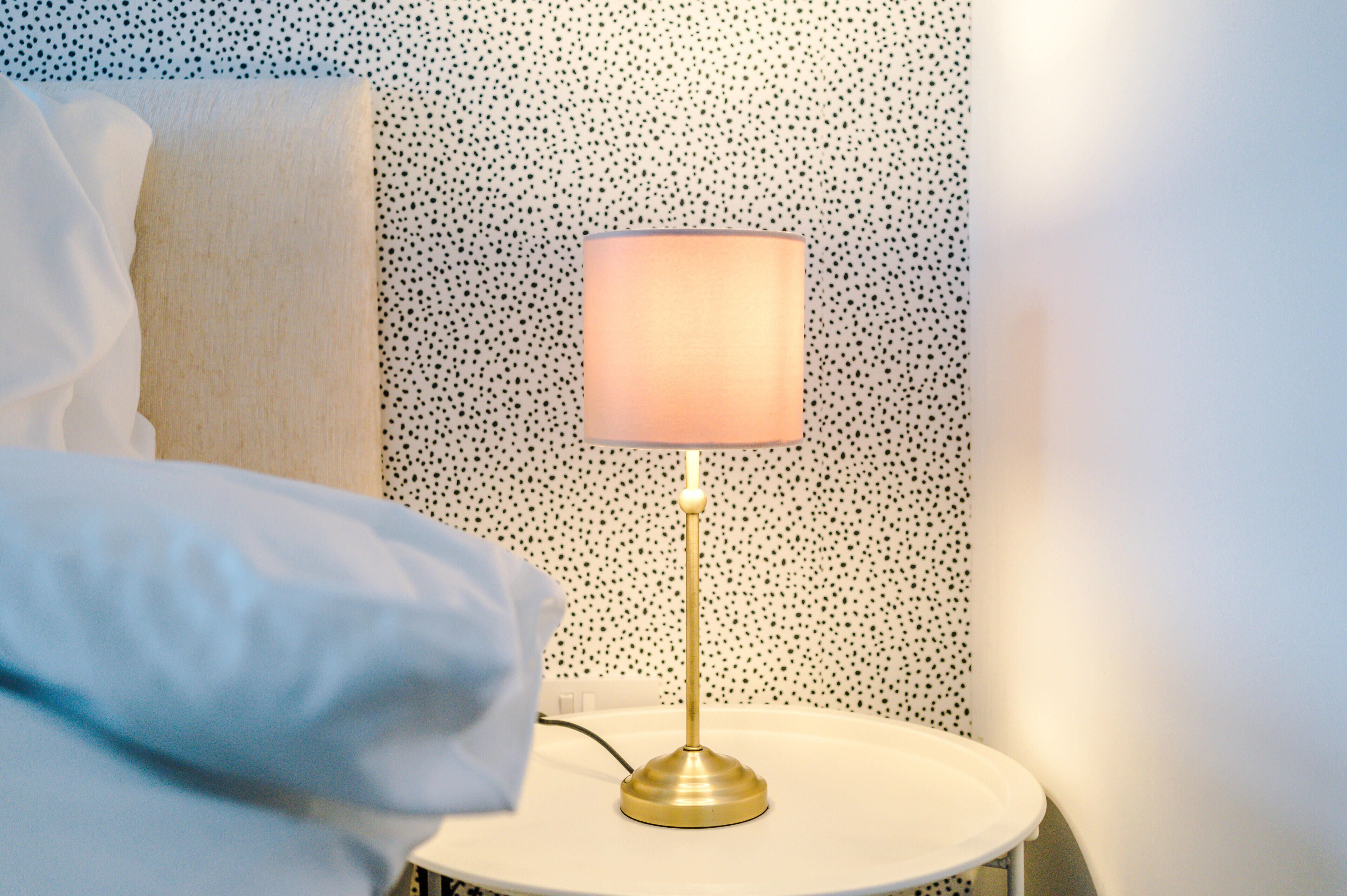 A bedside table with a lamp, a pillow, and a wall with a dotted pattern.