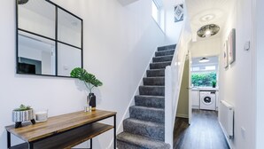 Eine Treppe führt zu einem Waschbereich, ein Holzkonsolentisch mit einer Pflanze und ein Spiegel an der Wand.