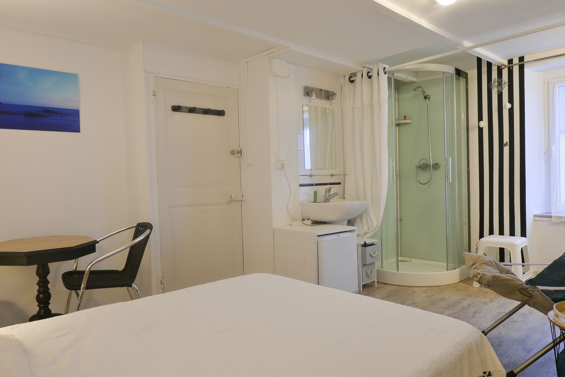 Habitación de hotel con cama, escritorio, silla, baño con ducha y un cuadro en la pared.