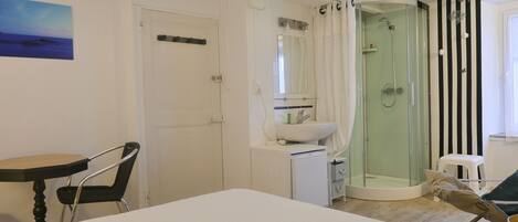 Habitación de hotel con cama, escritorio, silla, baño con ducha y un cuadro en la pared.