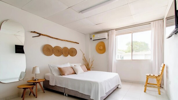 Une chambre à coucher avec un lit, une chaise en bois, un miroir rond et une fenêtre avec des rideaux.