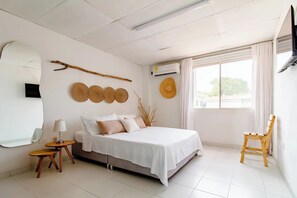 A bedroom with a bed, a wooden chair, a round mirror, and a window with curtains. - Apartment One street from the Beach Center Parque de los Novios (Santa Marta)