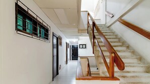 Un couloir avec un escalier, des murs blancs et un sol carrelé.