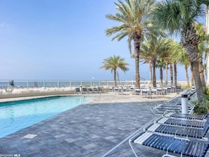 A poolside area with lounge chairs, palm trees, and a view of the ocean.
