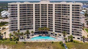 Ett stort hotell med flera balkonger, en central pool och utsikt över havet.