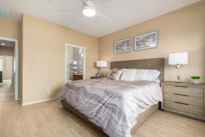 Un dormitorio con cama, mesitas de noche, cómoda, ventilador de techo y una obra de arte en la pared.