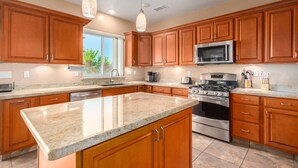 A modern kitchen with wooden cabinets, granite countertops, stainless steel appliances, and pendant lighting.