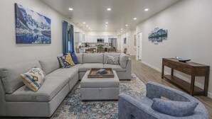 Un salon moderne avec un canapé d’angle gris, un petit pouf et un fauteuil bleu. Une console en bois, sur laquelle est posé un vase décoratif, est adossée au mur.