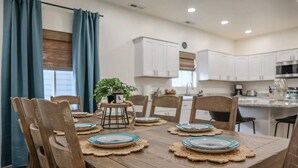 Un coin repas avec une table en bois dressée pour quatre personnes, entourée de chaises en bois. Une petite plante est posée sur un support au centre.