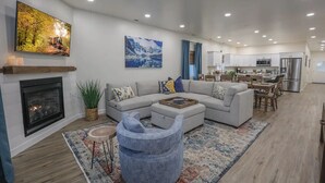 Un salon moderne avec une cheminée, un canapé d’angle, une table basse et un téléviseur fixé au mur.