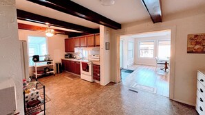 Cocina amplia con armarios de madera, un lavaplatos y una estufa. Se ve un comedor con una mesa y sillas a través de un umbral abierto.