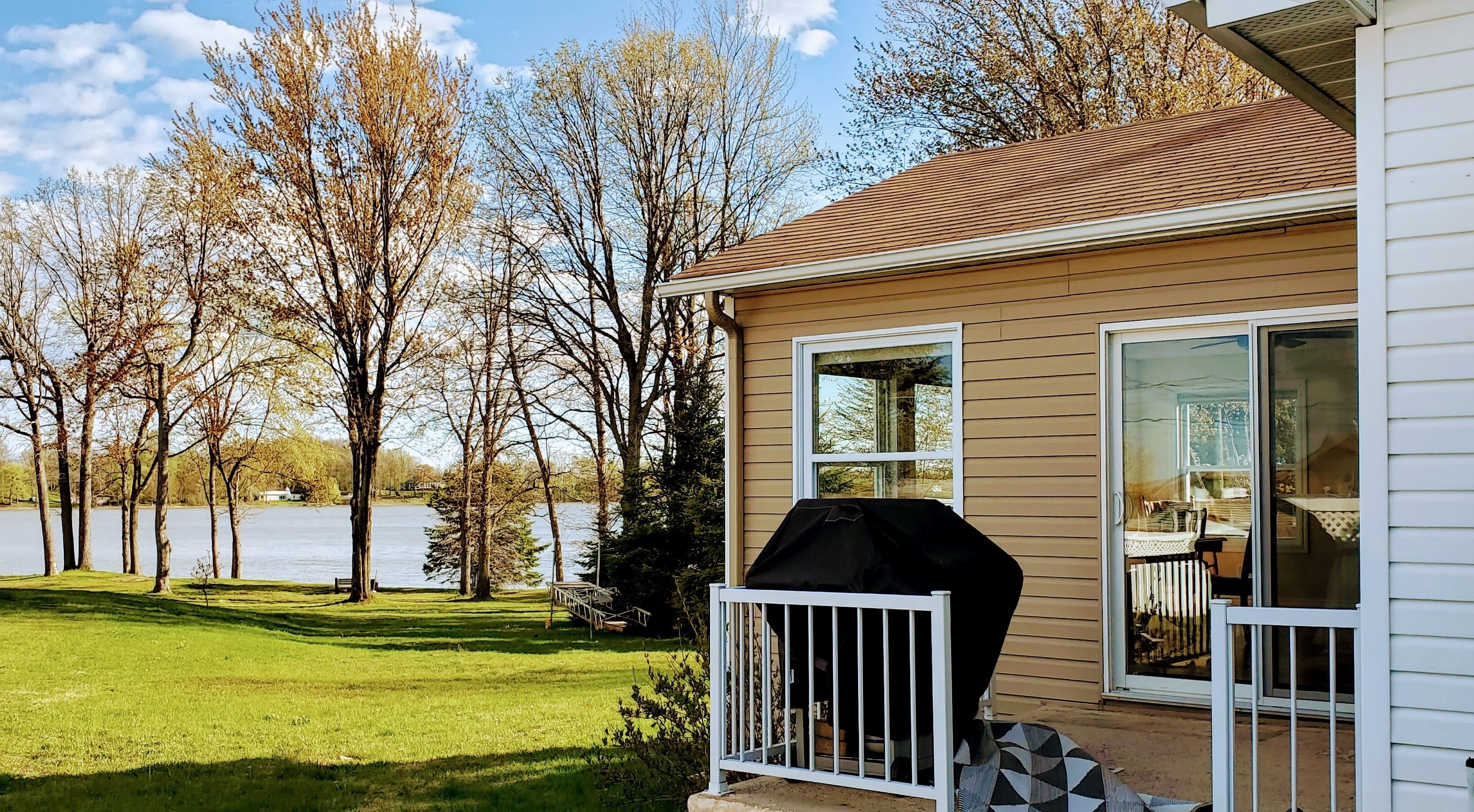 A house with a covered grill, a lawn, and a lake view.