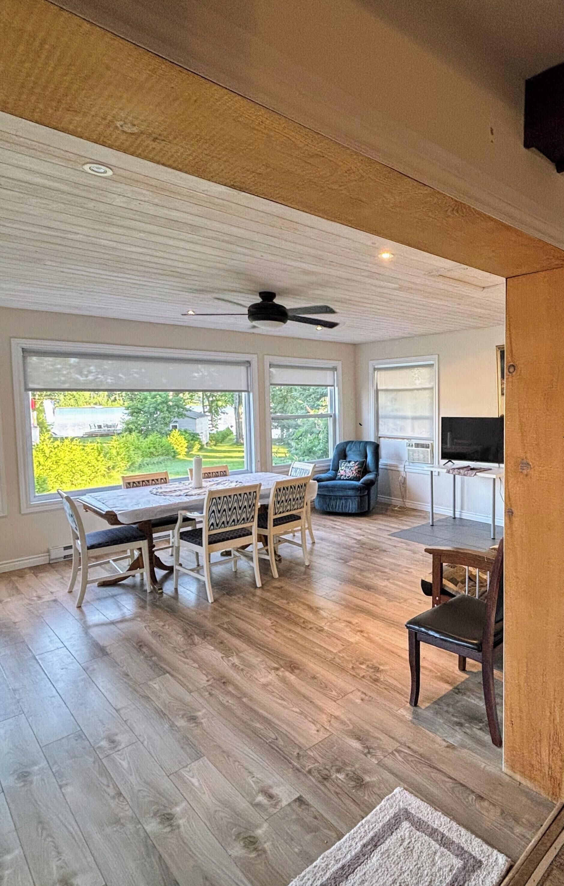 A spacious room with a dining table, chairs, a television, and a large window offering a view of greenery.
