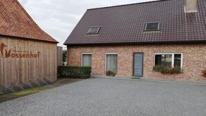 A brick building with a gravel driveway and a wooden structure labeled "Valkantiewoning Ossenhof". - Spacious quiet farmhouse between Lys and Scheldt, Belgium (Anzegem)