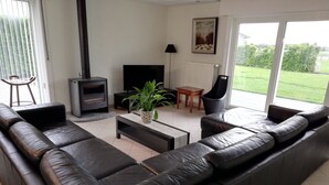 A modern living room with a black leather sofa, a fireplace, a TV, a plant, and a view of the outdoors. - Spacious quiet farmhouse between Lys and Scheldt, Belgium (Anzegem)
