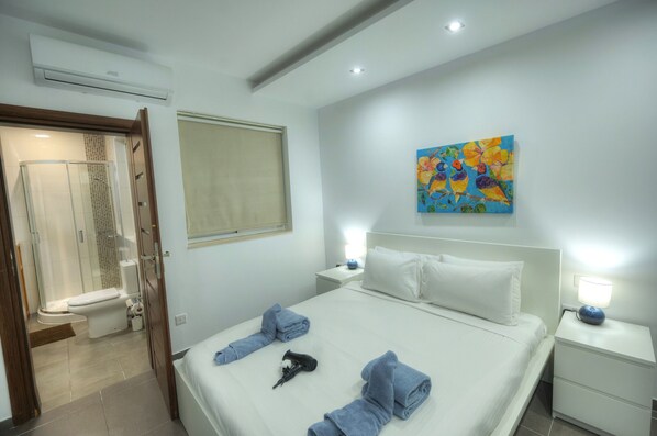 A hotel room with a bed, a nightstand, a painting, a window, and a shower area. - Bright & Large 2bedrooms in Sliema center MPOR1-1 (Sliema)