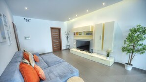 Ein modernes Wohnzimmer mit grauem Sofa, orangefarbenen Kissen, einem Flachbildfernseher und einem Topf mit Pflanze.
