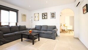 A modern living room with a grey sectional sofa, a coffee table with fruit, and a dining area with a white table and chairs. - 3 Bedroom Apartment, 40m to the beach Puerto Pollensa (Puerto Pollensa)