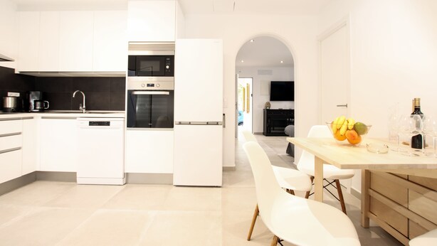 A modern kitchen with white cabinetry, a built-in oven, and a dining area with a wooden table and white chairs. - 3 Bedroom Apartment, 40m to the beach Puerto Pollensa (Puerto Pollensa)