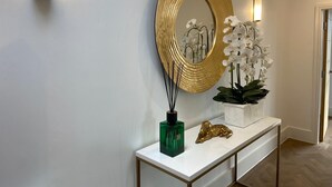 A hallway with a white console table, a gold-framed mirror, white orchids, a green vase, and a gold statue. - A 2 bedroomed penthouse with large bi-fold doors accessing a good sized decked balcony area with stu (York)