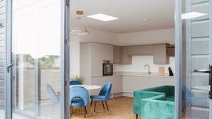 A modern kitchen with a built-in oven and a sink, a dining area with a round table and blue chairs, and a teal sofa. - A 2 bedroomed penthouse with large bi-fold doors accessing a good sized decked balcony area with stu (York)