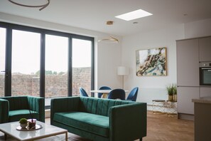 Un salon moderne avec un canapé vert, une table basse et une vue sur la ville grâce à de grandes fenêtres.
