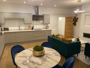 Une cuisine moderne avec des meubles blancs, un îlot central et un coin repas comprenant une table ronde et des chaises bleues.