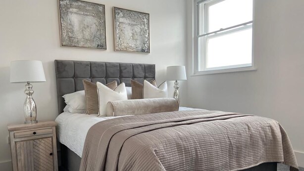 A bedroom with a bed, two bedside tables, and two wall-mounted abstract paintings. - A 2 bedroomed penthouse with large bi-fold doors accessing a good sized decked balcony area with stu (York)