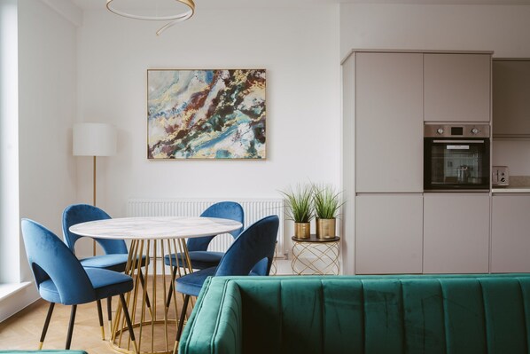 Une cuisine moderne dotée d’un four encastré et d’un coin repas avec une table ronde et des chaises bleues.