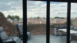 A balcony with a view of a town, featuring a brick wall, a table, and two chairs. - A 2 bedroomed penthouse with large bi-fold doors accessing a good sized decked balcony area with stu (York)