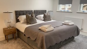 Un lit bien fait, avec une couverture grise, des oreillers et des serviettes pliées.
