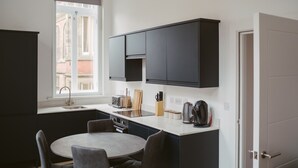 A compact kitchen with dark cabinets, a built-in oven, a sink, and a round dining table with chairs. - Apartment 3 (1 bedroom, sleeps x 4) (York)