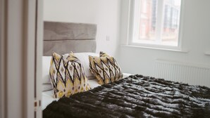 A bedroom with a bed, patterned pillows, a black blanket, and a window with a view of buildings. - Apartment 3 (1 bedroom, sleeps x 4) (York)