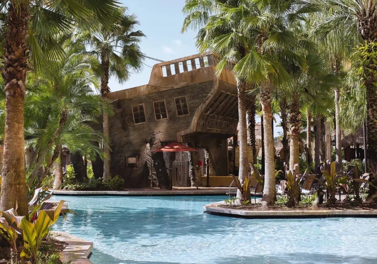 A pool area with palm trees and a stone building with arched windows.